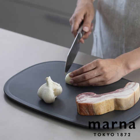 marna TOKYO 1872 品牌下，廚師正在防刮防滑砧板上切洋蔥，旁邊放著一塊培根和一顆大蒜。