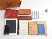 職人手作皮革屋瓦風兩用單肩包 (CW-3) 搭配多種配件，包含棕色皮革單肩包、紅色皮革小包、橘棕色皮夾、咖啡色筆袋、白色藍條紋毛巾、一瓶水、平板電腦、手機、筆記本和多本文件夾，展示豐富的收納功能。