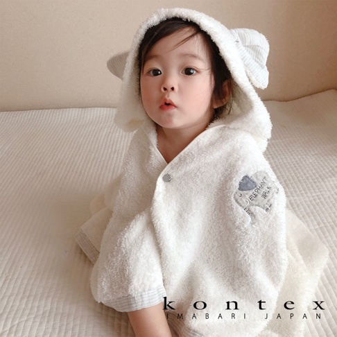 一名嬰幼兒穿著今治純棉連帽浴巾，浴巾為白色，材質柔軟蓬鬆，帶有可愛的動物造型連帽，左胸前繡有大象圖案與英文文字，袖口有灰色細條紋。