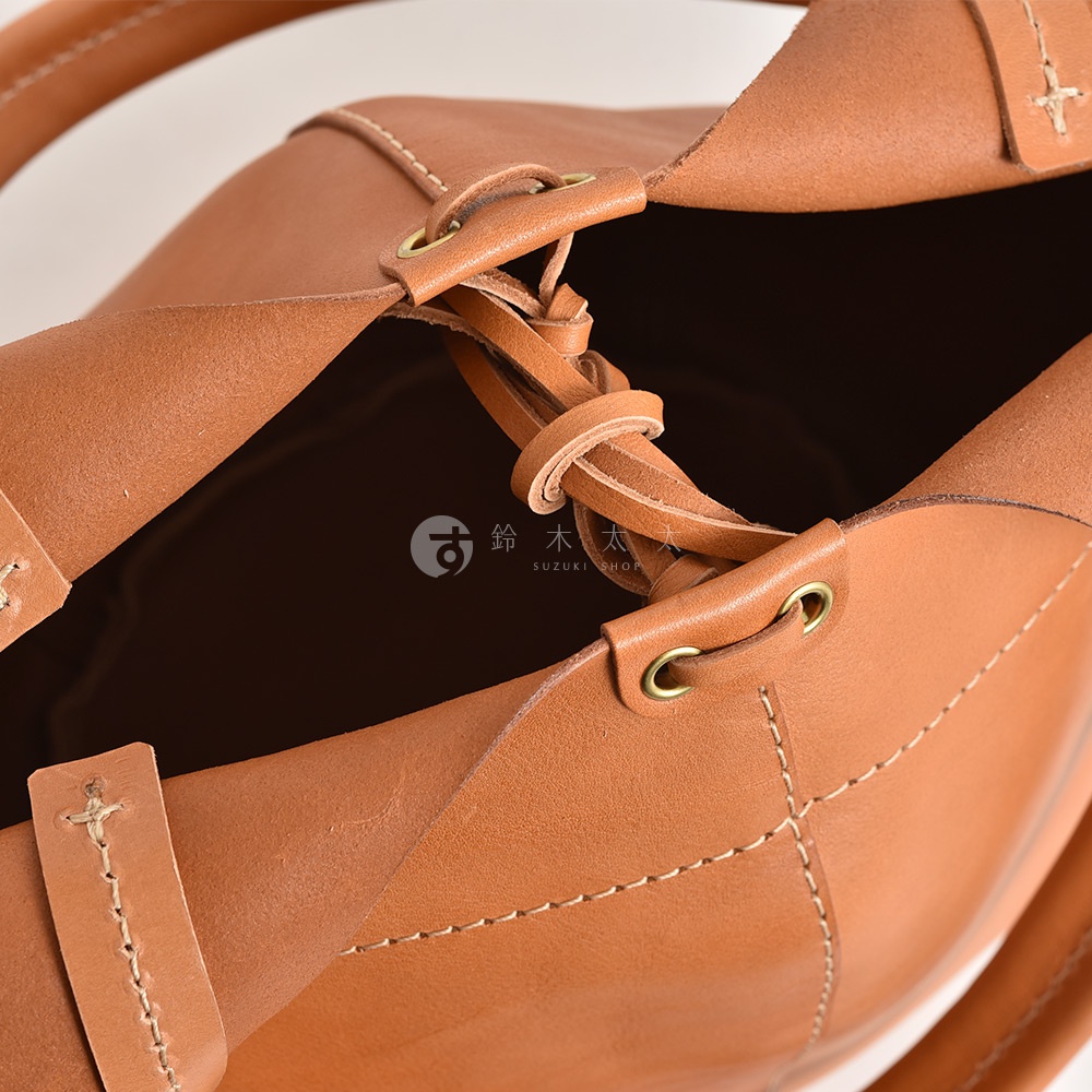 職人手作皮革球形肩掛托特包，展示棕褐色皮革材質，包身縫線細緻，採用抽繩閉合設計，搭配金屬孔眼與皮革綁帶。