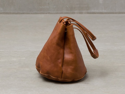 棕色皮革製成的抽繩托特包，具有圓潤的底部和兩條皮革提把。