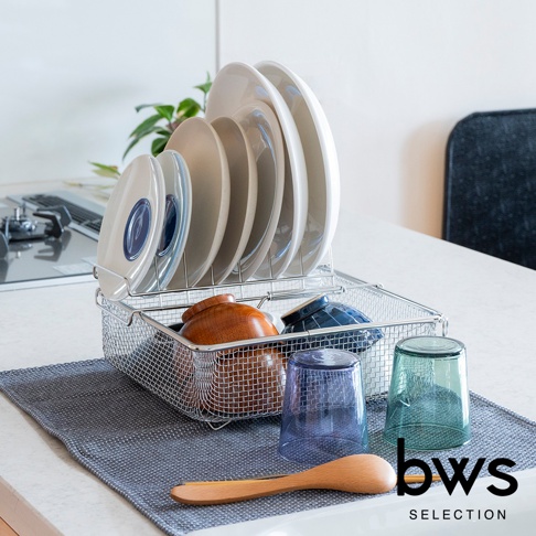 bws SELECTION 的不鏽鋼可伸縮簡約瀝水架，架上擺放著多個白色盤子，下方籃子裡有木碗和藍色碗，旁邊放著藍綠色玻璃杯和木製湯匙