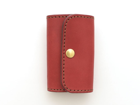 紅色皮革經典鑰匙包，配有六個鉤子和一個黃銅按扣，以咖啡色縫線手工製作，整體設計簡潔。