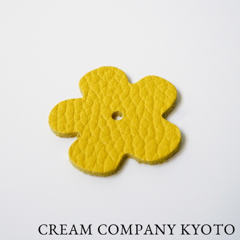 一個黃色皮革製成、五瓣花朵造型的吊飾，帶有圓形孔洞。