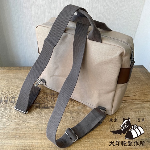 犬印純綿帆布三用橫式側背包，米白色帆布材質，搭配深棕色皮革飾邊，設有兩條灰色寬版織帶提把及一條可拆卸肩背帶。