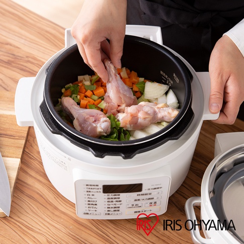 白色電子壓力鍋內有雞腿、胡蘿蔔塊、芹菜塊和洋蔥塊，上方有一雙手正在放入雞腿。