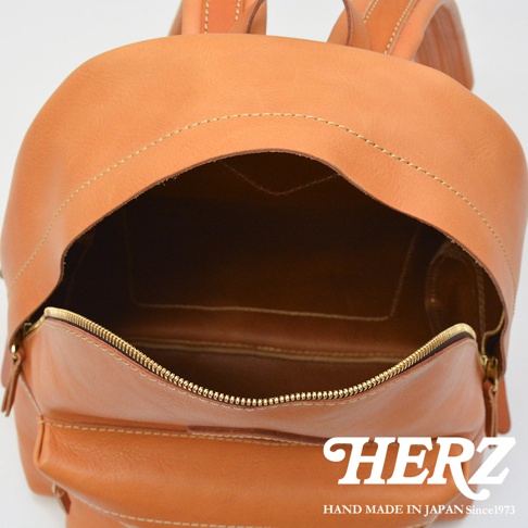 淺棕色皮革後背包，頂部拉鍊敞開，露出內部空間。包身有縫線裝飾，材質為真皮。
