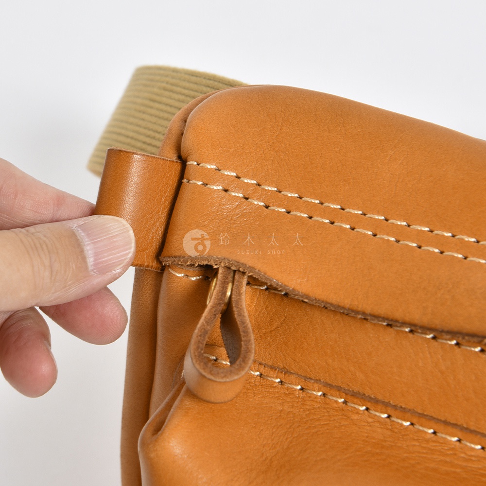 皮革製成的棕色兩用腰掛斜背包，特寫展示了包包的縫線細節、拉鍊和連接帶。