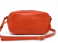 亮橘色皮革製成的隨身單肩小包，方形設計，頂部有拉鍊開口，附有可調節長度的細肩帶及金色金屬調整環。