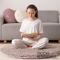 一位女士坐在圓形涼感夾心包覆圓墊上閱讀。圓墊為大地色系，表面有立體紋理。背景為灰色沙發，上方擺放著粉色和米白色的圓形靠墊。