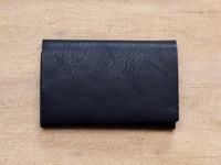 黑色皮革薄型名片夾，表面紋理清晰，置於淺色木紋背景上。