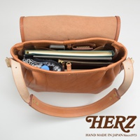 職人手作皮革大容量扣環郵差包，棕色皮革，內有手機、筆記本、錢包、水瓶和衣物。