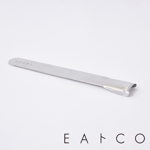 日製不鏽鋼玉米刨刀，長條狀金屬本體，一端為彎曲設計，帶有鋸齒狀邊緣，用於刨取玉米粒。