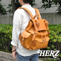 職人手作皮革復古風旅行後背包，採用天然皮革材質，呈現經典棕褐色。設計包含翻蓋主袋、束繩開口、側邊翻蓋口袋，並搭配金屬扣環與縫線細節。