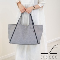 一位女士手持一個藍白格紋刺子織托特包，包邊為深藍色，有兩個肩帶，包口有一個銀色按扣。