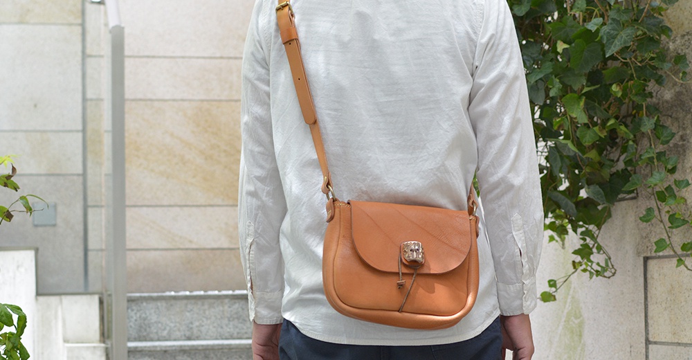 簡約風格的棕色皮革肩背包，配有鹿角造型金屬扣和抽繩，適合日常搭配。