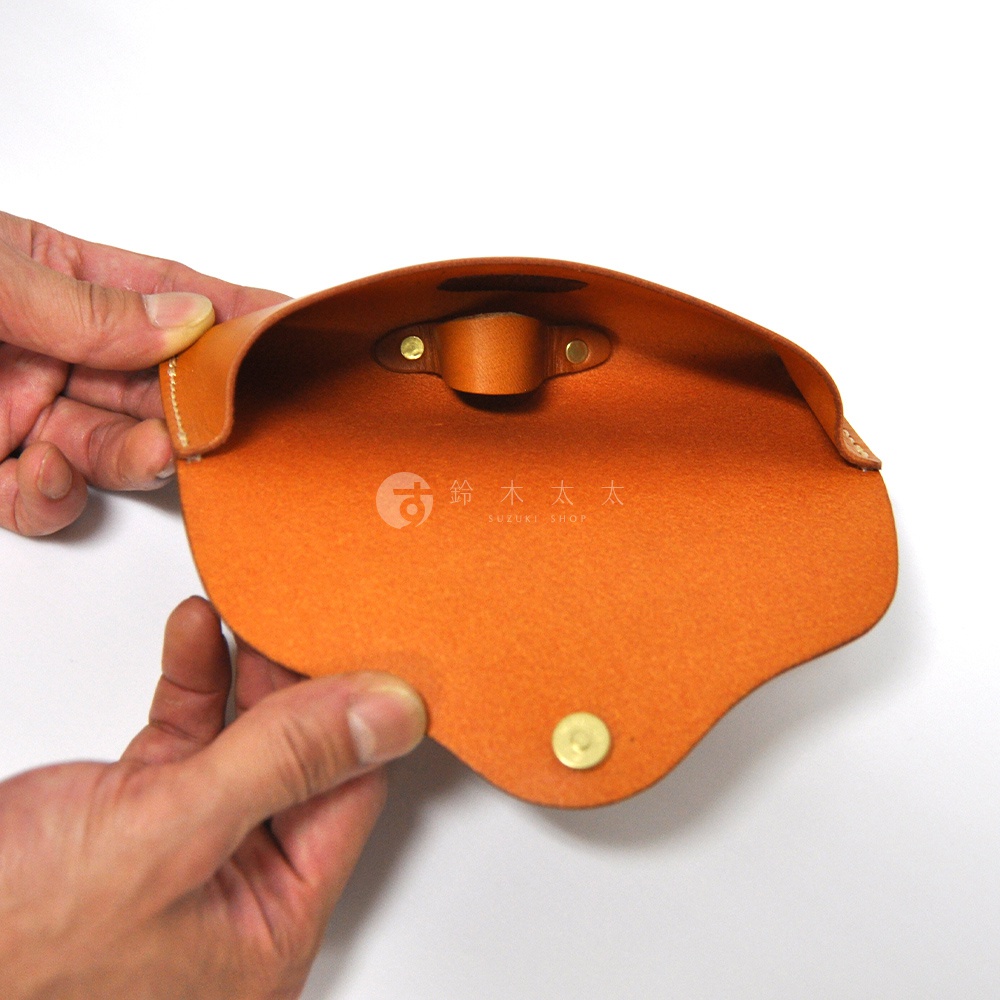 皮革眼鏡收納盒，橘色皮革，內部有品牌標誌，由雙手持握展示。