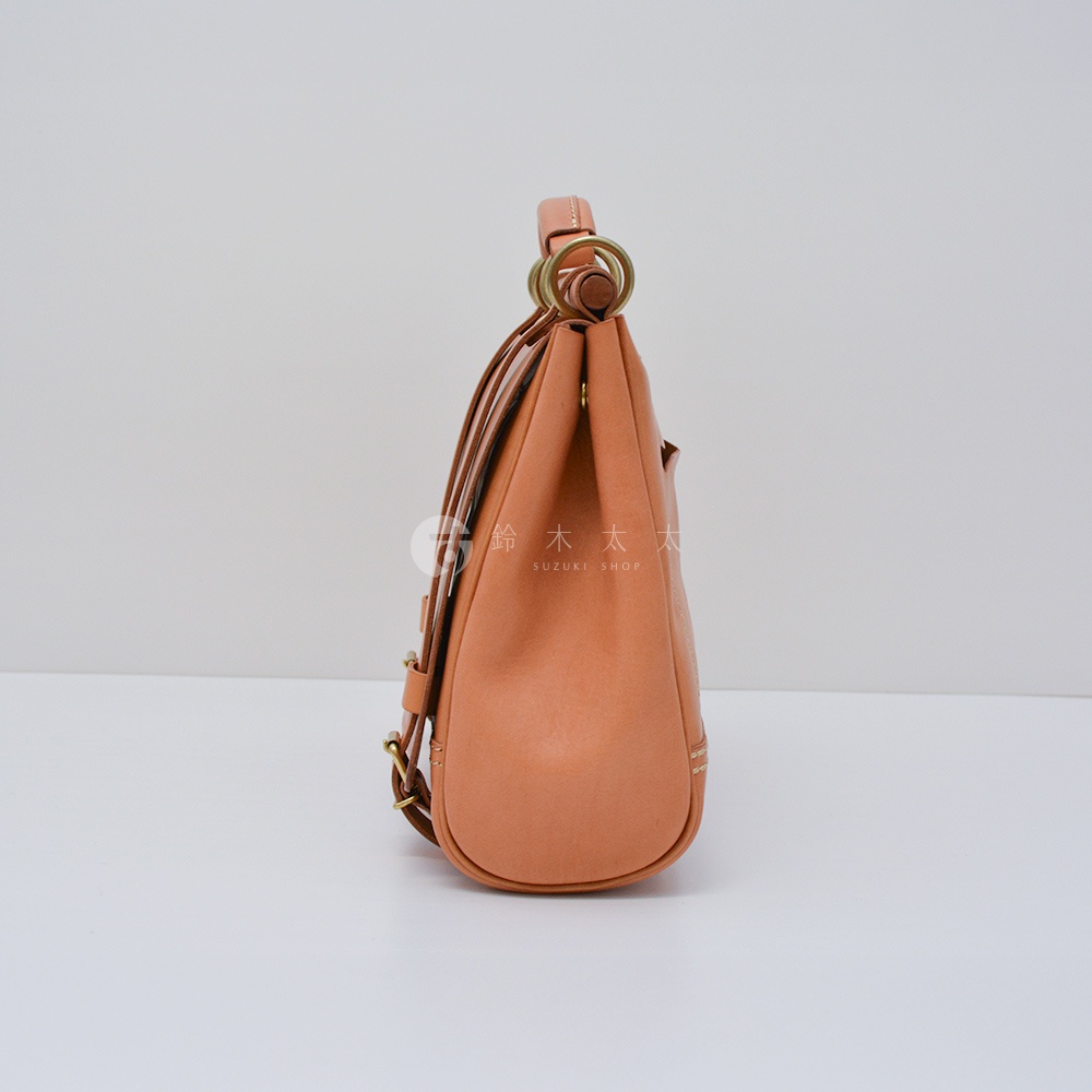 日本HERZ職人手作皮革屋瓦風側背包 CW-147，從側面看，呈現粉橙色皮革的飽滿質感，搭配金屬環扣與提把，設計簡約而精緻。