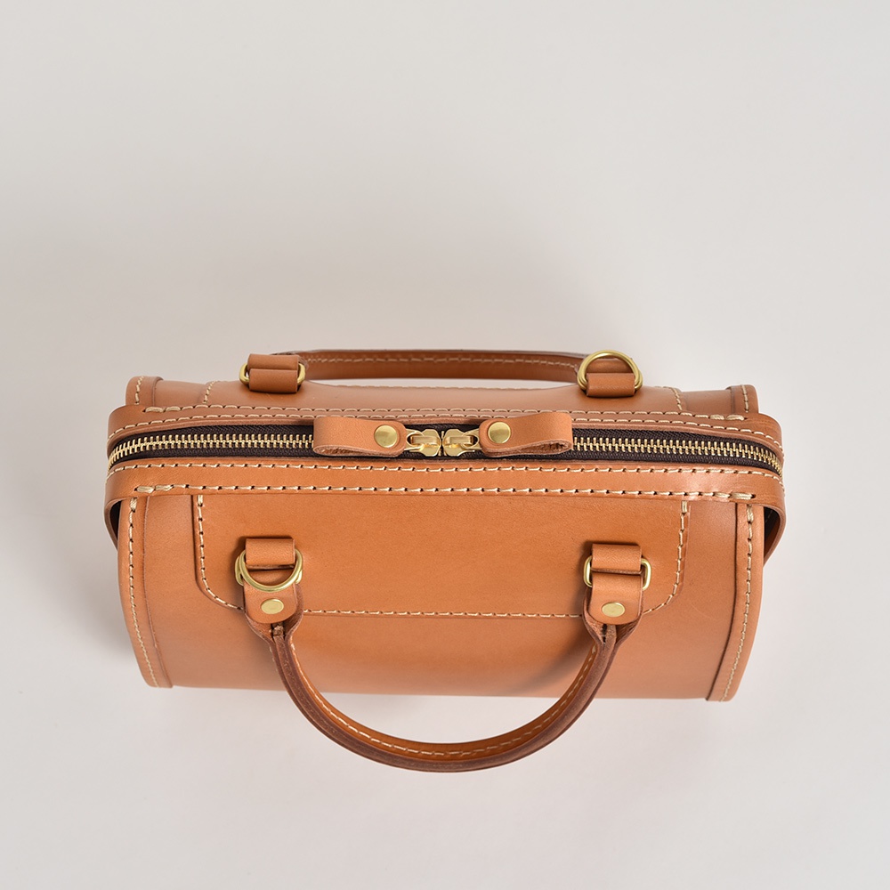 職人手作皮革迷你波士頓包，呈現自然棕色，採用高品質皮革製成，搭配黃銅色拉鍊和五金配件，細緻縫線展現精湛工藝。