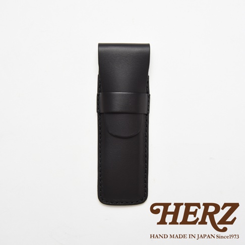 一個黑色皮革製成的HERZ品牌職人手作單支鋼筆收納筆袋，採用簡約的翻蓋式設計並搭配皮革固定環，外觀呈現霧面質感，底部印有HERZ品牌名稱與手工製造相關說明。