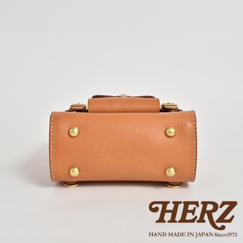 職人手作皮革經典學院風迷你後背包 R-24，展示原色皮革材質，包身設有金屬卯釘及皮革提把，底部有四個金屬腳釘。