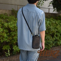 黑色皮革製的職人手作兩用手機包，斜背於穿著淺藍色襯衫和褲子的模特兒身上。