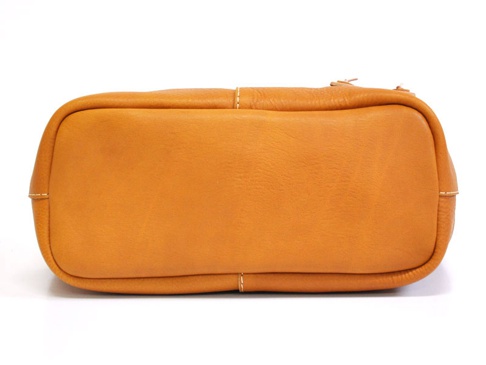 職人手作皮革托特包，呈現溫暖的焦糖棕色，材質為柔軟皮革，包身結構飽滿，側邊及底部有細緻的白色縫線，展現精湛工藝。