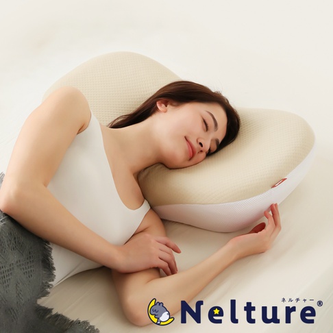 一位女性側臥在乳白色、帶有紋理的NELUD 完美釋壓Q彈棉花糖枕上，枕頭呈現流線型設計，邊緣有網狀透氣材質，整體營造出舒適的睡眠氛圍。