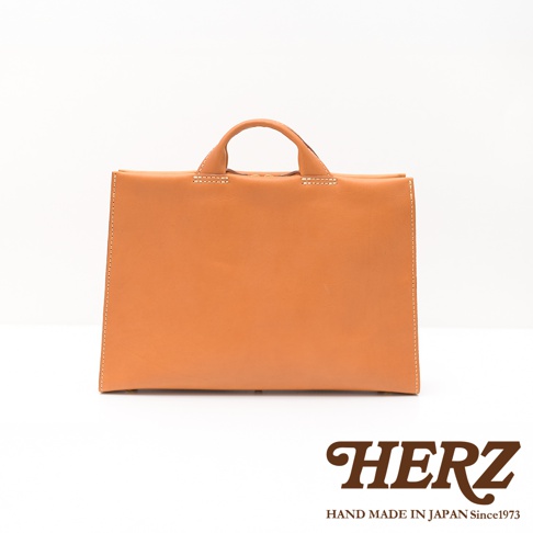 日本HERZ手工皮革簡約商務公事包，橘色皮革，附提把，白色縫線，底部有支撐腳，下方有HERZ品牌Logo及Hand Made in Japan Since1973字樣