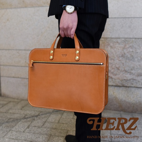 職人手作皮革兩用商務公事包，採用棕色皮革，搭配金色拉鍊和鉚釘，設計簡潔大方。