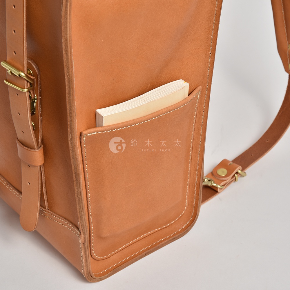 職人手作棕色皮革後背包，右側有一個插入薄書本的收納袋，配有銅質金屬扣件及可調式皮質背帶。