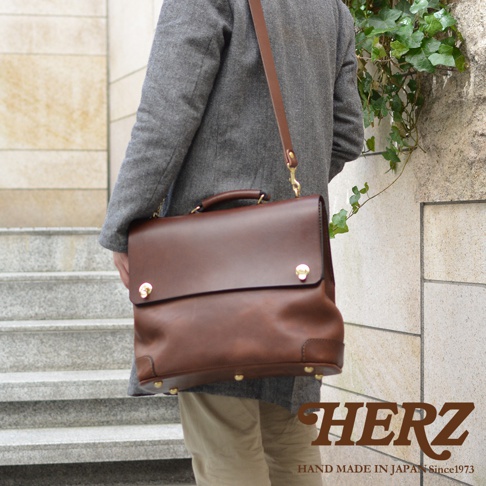 深棕色皮革旅行商務兩用波士頓包，有頂部提把和可拆卸肩帶，金色旋轉鎖扣和底部釘腳。