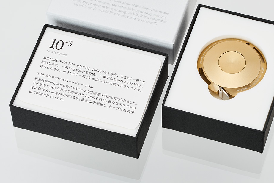 金色鋁製卷尺，1.5M，圓形設計，置於黑色禮盒內的白色襯墊中，盒蓋上印有日文說明。