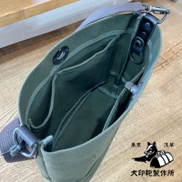 一個綠色純棉帆布迷你側背包，內部有夾層和磁扣，搭配灰色帆布肩帶和黑色皮革裝飾。