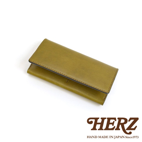 日本HERZ職人手作皮革翻蓋長夾，採用橄欖綠色皮革製作，外觀簡約素雅，呈現細膩的質感與職人縫線細節，底部附有HERZ品牌標誌與說明文字。