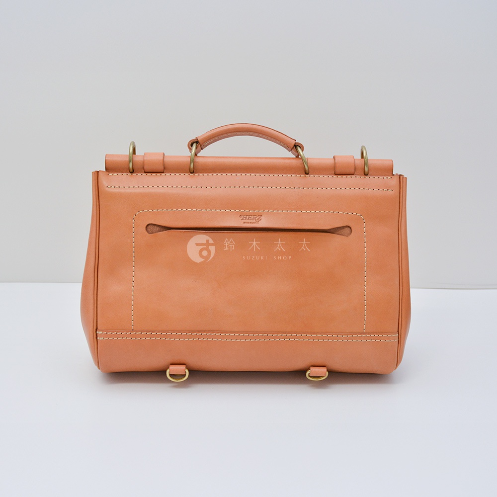 日本 HERZ 職人手作皮革屋瓦風側背包 CW-147 淺棕色，正面有兩個銅環和一個手提把，中間有拉鍊口袋，上方印有 HERZ LOGO 及 SUZUKI SHOP 字樣。