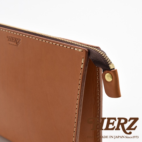 職人手作皮革三角底拉鍊手拿包，採用棕色皮革，配有復古風格的黃銅拉鍊和壓扣，縫線明顯。