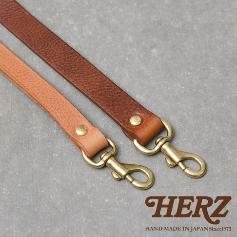 HERZ 品牌標誌和「HAND MADE IN JAPAN Since1973」字樣，下方展示兩條不同顏色的皮革背帶，上方為深棕色，下方為淺棕色，兩條背帶末端均配有金色登山扣。