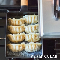 黑色的琺瑯鑄鐵玉子燒鍋，鍋內擺放著七個煎至底部金黃的日式煎餃，鍋柄為木質。