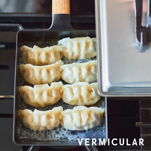 黑色的琺瑯鑄鐵玉子燒鍋，鍋內擺放著七個煎至底部金黃的日式煎餃，鍋柄為木質。