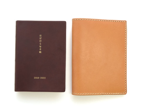 深棕色皮革書套，表面有金色日文文字「ほぼ日 5年手帳」及「2018-2022」字樣。右側為淺棕色皮革書套，邊緣有白色縫線。