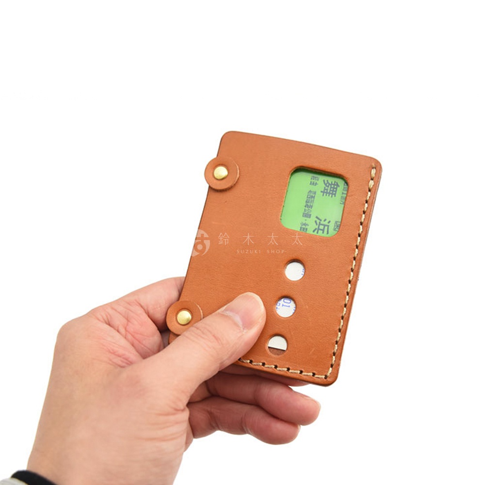 以手持的方式展示日本 HERZ 品牌皮革交通卡收納夾，卡夾為淺棕色皮革，上面有兩個鉚釘裝飾，並可見部分綠色交通卡。