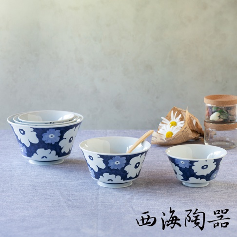 波佐見燒藍花紋三件式丼飯碗，白色陶瓷碗身印有藍色花朵圖案，大小堆疊擺放，其中一個碗內有一支木湯匙，背景為淺灰色牆面與淺藍色桌布。