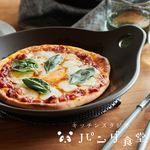 Kitchen Studio Panda食堂的多用途耐熱料理盤上放著一個裝飾著羅勒葉的瑪格麗特披薩