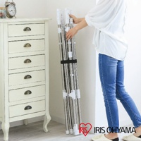 摺疊狀態的雙桿不鏽鋼曬衣架，銀色金屬桿身，附有白色連接件和黑色束帶，旁邊是一件米白色六抽屜矮櫃，左上方有一個復古鬧鐘。