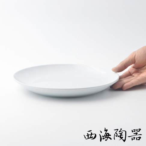 一個白色的波佐見燒 Common 陶瓷料理盤，直徑 24 公分，盤面平坦，邊緣略微向上彎曲。一隻手輕輕握住盤子的邊緣。