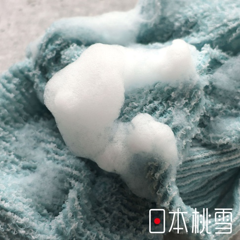 日本桃雪 logo 標誌浮在細緻柔軟的藍色毛巾上，毛巾紋理清晰，觸感蓬鬆，充滿細密泡沫。