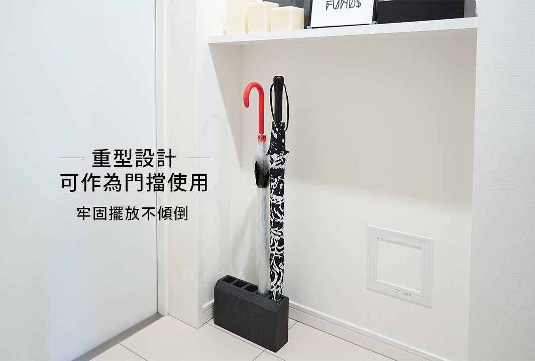 黑色砂岩材質的五孔傘架，上面插著兩把傘，一把是紅色彎柄的，另一把是黑白圖案的。傘架造型簡約，可作為門擋使用，穩固不傾倒。