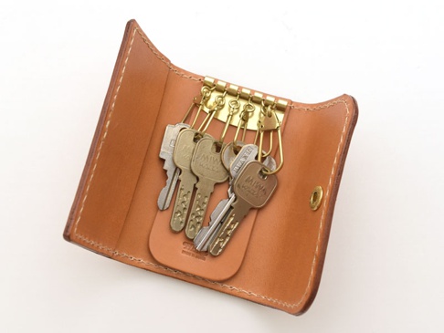 淺棕色皮革製作的六鉤鑰匙包，內有五把銀色和黃銅色鑰匙，鑰匙包的邊緣有縫線裝飾，並有一個金色按扣。
