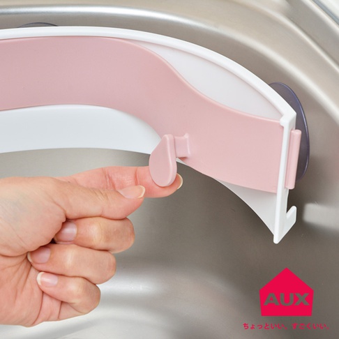 粉色塑膠製的開合式流理台廚餘架，邊緣為白色，一側配有紫色吸盤固定，手正操作其鎖扣。